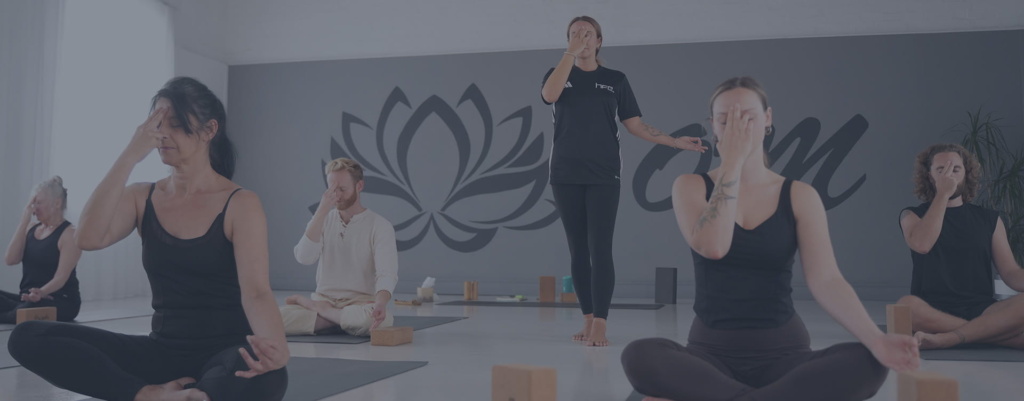 A female yoga instructor teaching a class as students sit crossed legged on their mats