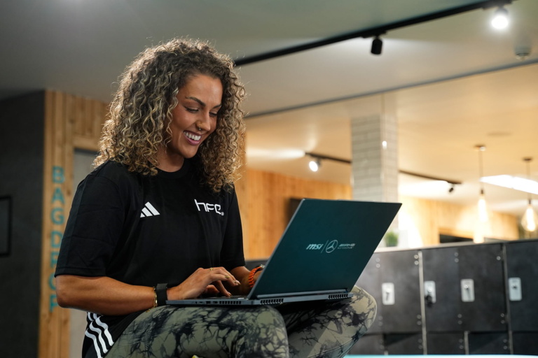 A female PT sat on her laptop in a gym environment