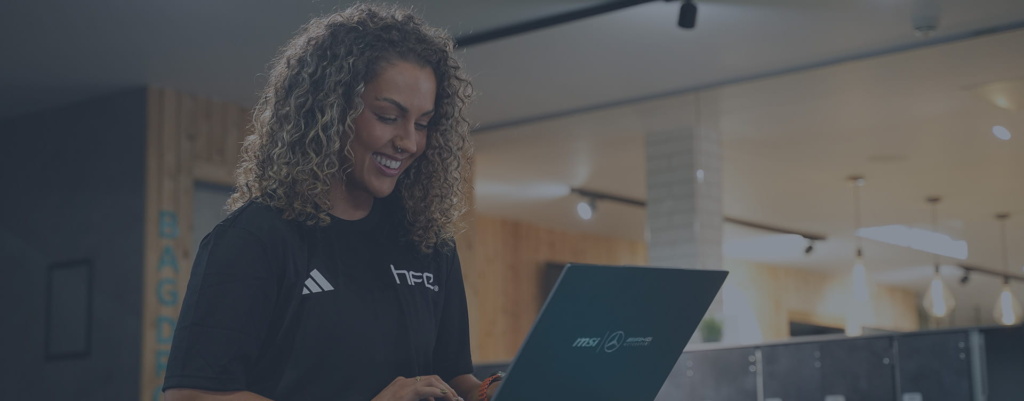 A female PT sat in a gym environment on her laptop