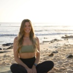 Nicole Ann McGillivray sat on a beach cross-legged smiling